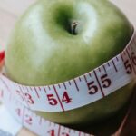 Fitness Nutrition - Green apple with measuring tape on table in kitchen