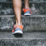 Exercise - person wearing orange and gray Nike shoes walking on gray concrete stairs