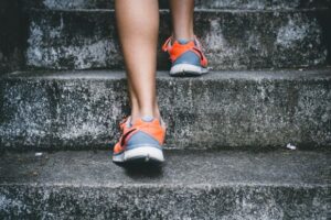 Exercise - person wearing orange and gray Nike shoes walking on gray concrete stairs