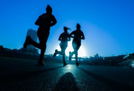 Exercise - silhouette of three women running on grey concrete road