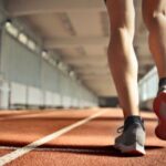 Leg Exercises - From below back view of crop strong runner walking along running track in athletics arena while doing warm up exercises during workout