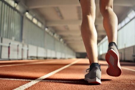 Leg Exercises - From below back view of crop strong runner walking along running track in athletics arena while doing warm up exercises during workout