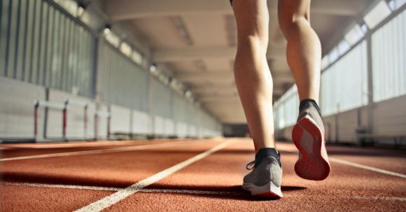 Leg Exercises - From below back view of crop strong runner walking along running track in athletics arena while doing warm up exercises during workout